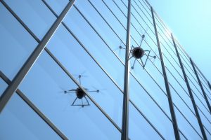Quadrocopter unmanned aerial vehicle, or UAV, powered by four individual rotors giving it agility and increased maneuverability for surveillance work, flying overhead against a window with blue sky